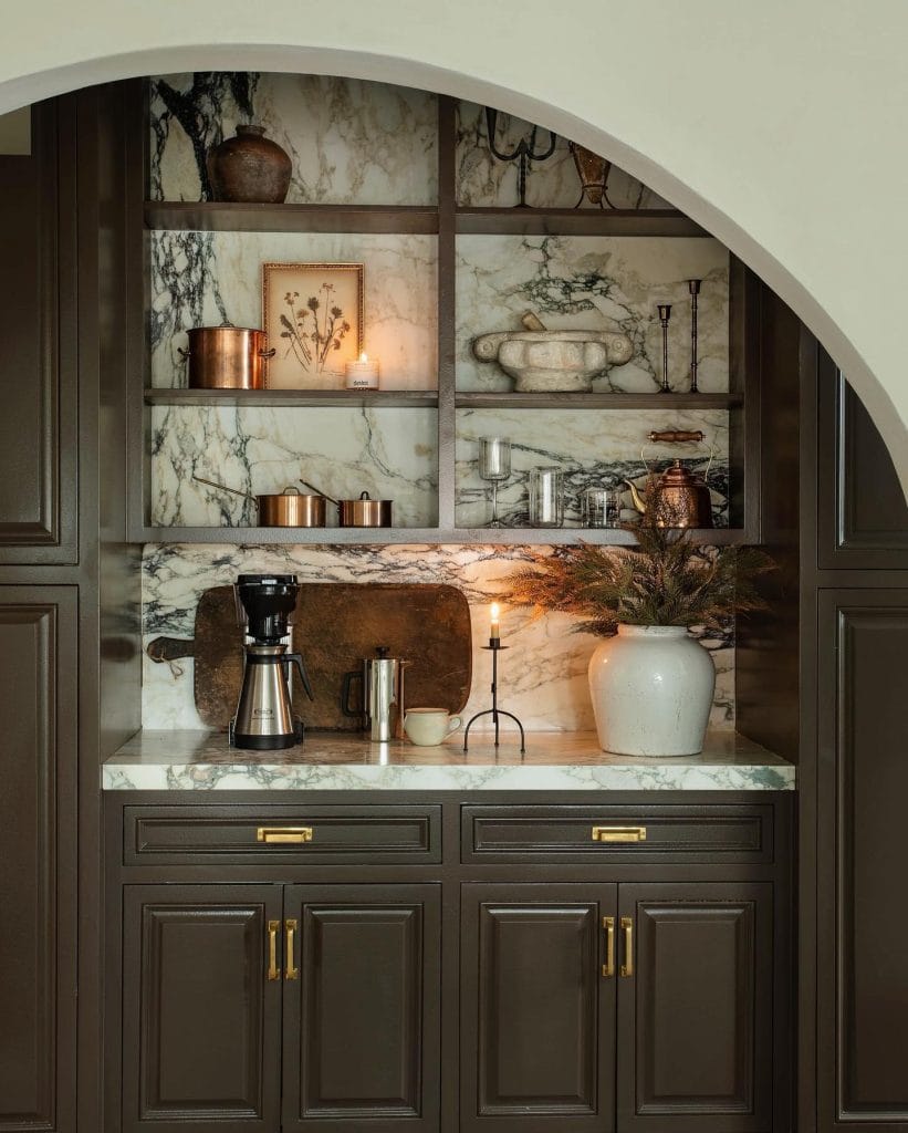 Luxurious coffee bar with dark cabinetry, marble backsplash, metal accents, and rustic decor pieces.