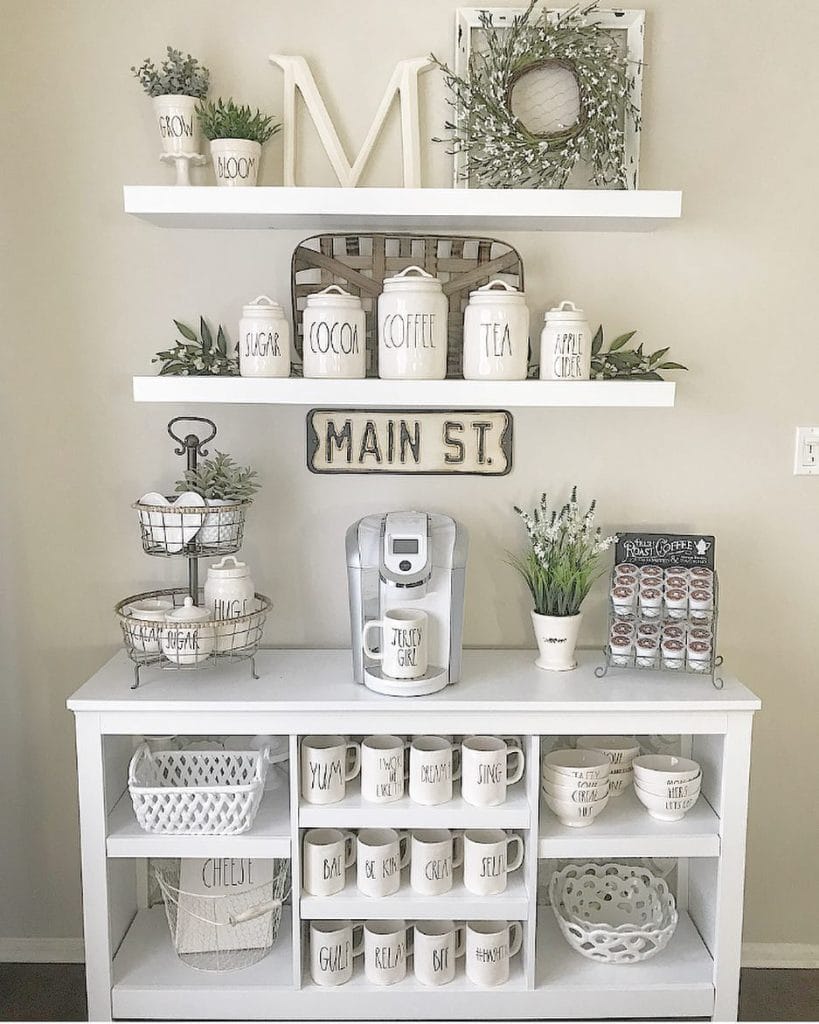 Bright and airy coffee bar with white cabinetry, shelves adorned with greenery, and ceramic canisters.