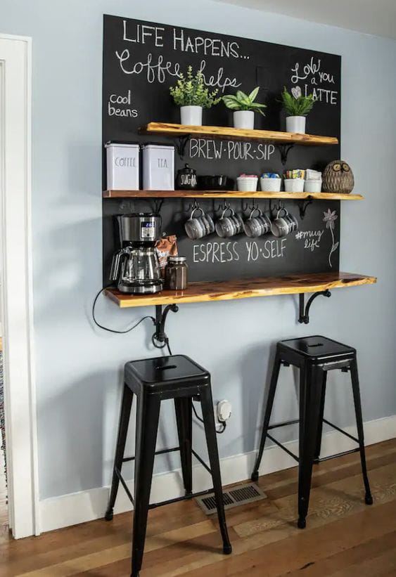 Compact coffee bar with vertical storage shelves, a chalkboard backdrop, and bar stools underneath for small spaces.