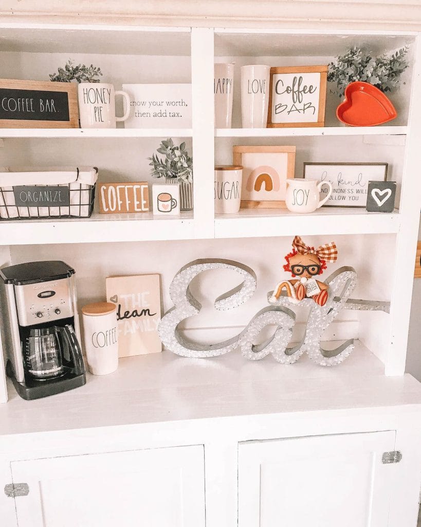 Charming home coffee setup with Rae Dunn-inspired mugs, cheerful signage, and open shelving.