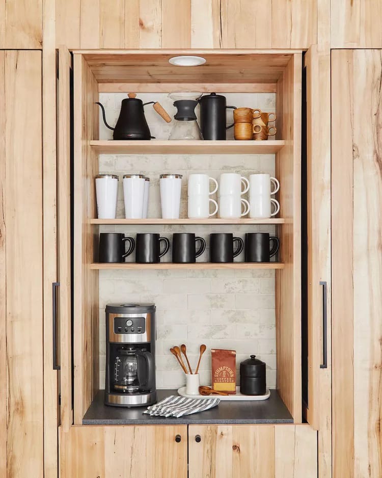 Modern, minimalist coffee nook hidden behind pocket doors with black and white mugs against a light wood backdrop.