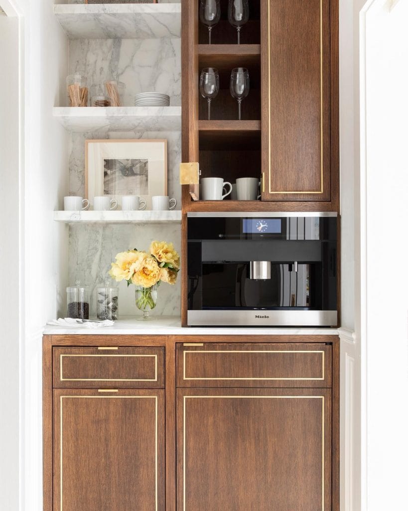 Luxurious coffee station with marble countertops, rich wooden cabinetry, and brass hardware.