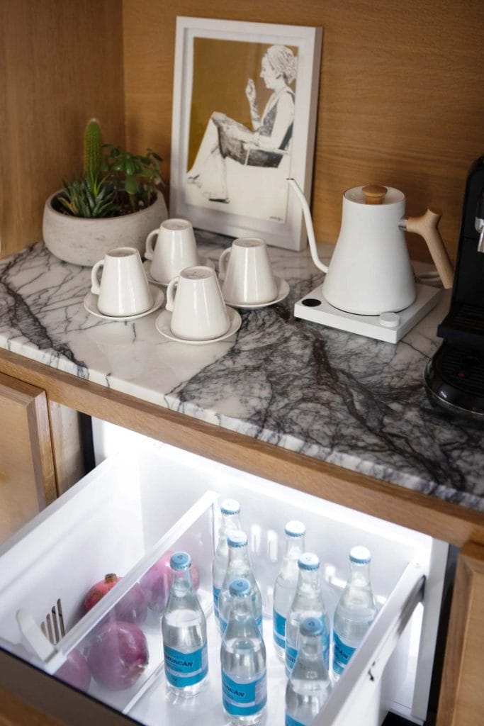 Sleek, modern coffee nook with mini-fridge, marble countertop, and white kettle.