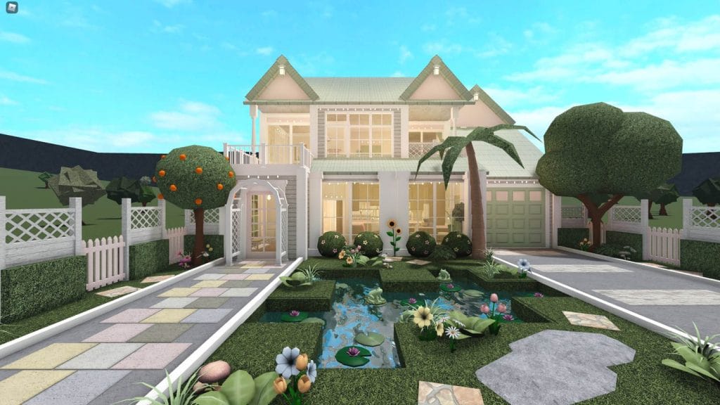 A cozy two-story home with a soft green exterior, white trim, and a charming front garden featuring a small pond and a variety of colorful flowers.