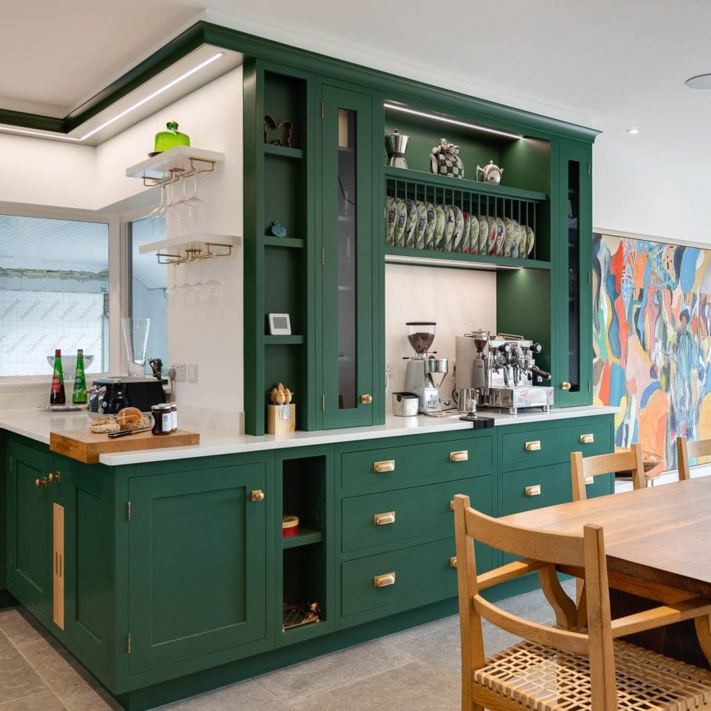 Dark green cabinetry with brass hardware, white countertop, espresso machine, and grinder.