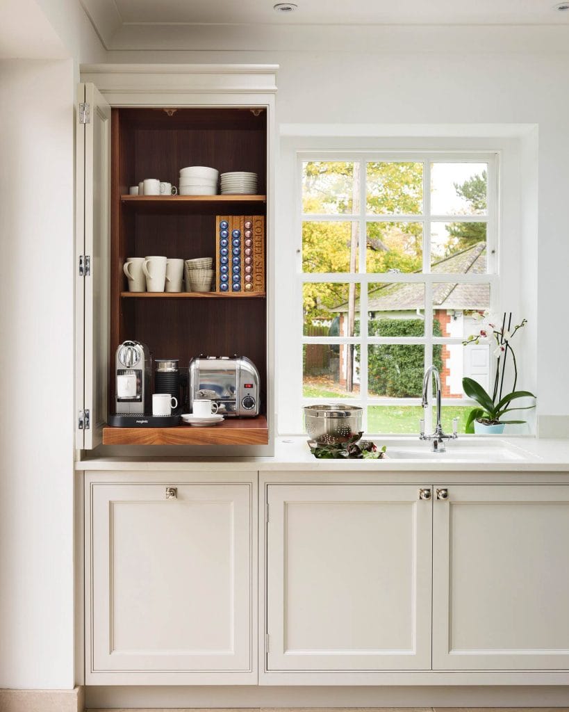 Discreet coffee station behind cabinet doors, revealing organized shelves and coffee-making appliances.