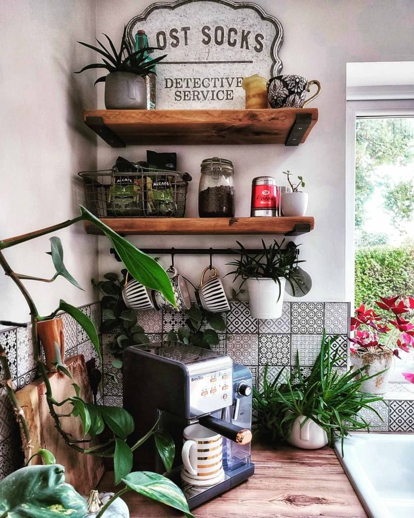 Coffee station with lush greenery, wood and metal accents, and eclectic mix of mugs and coffee jars.