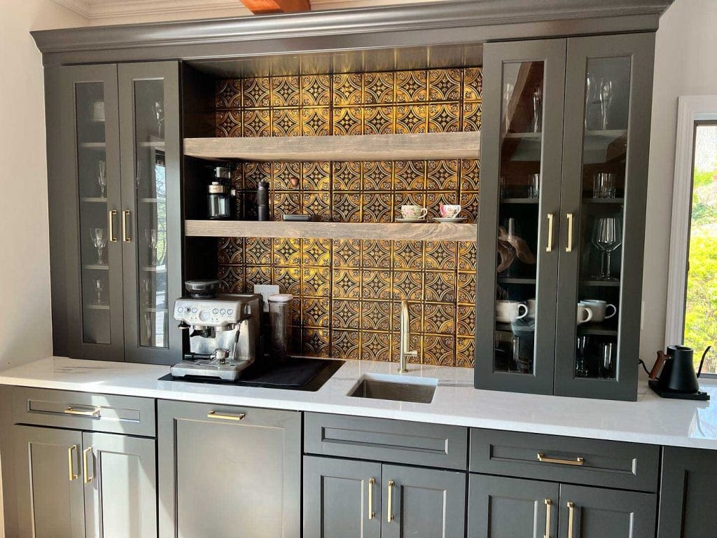 Elegant coffee station with dark cabinetry, striking tile backsplash, built-in shelves, and glass-front cabinets.