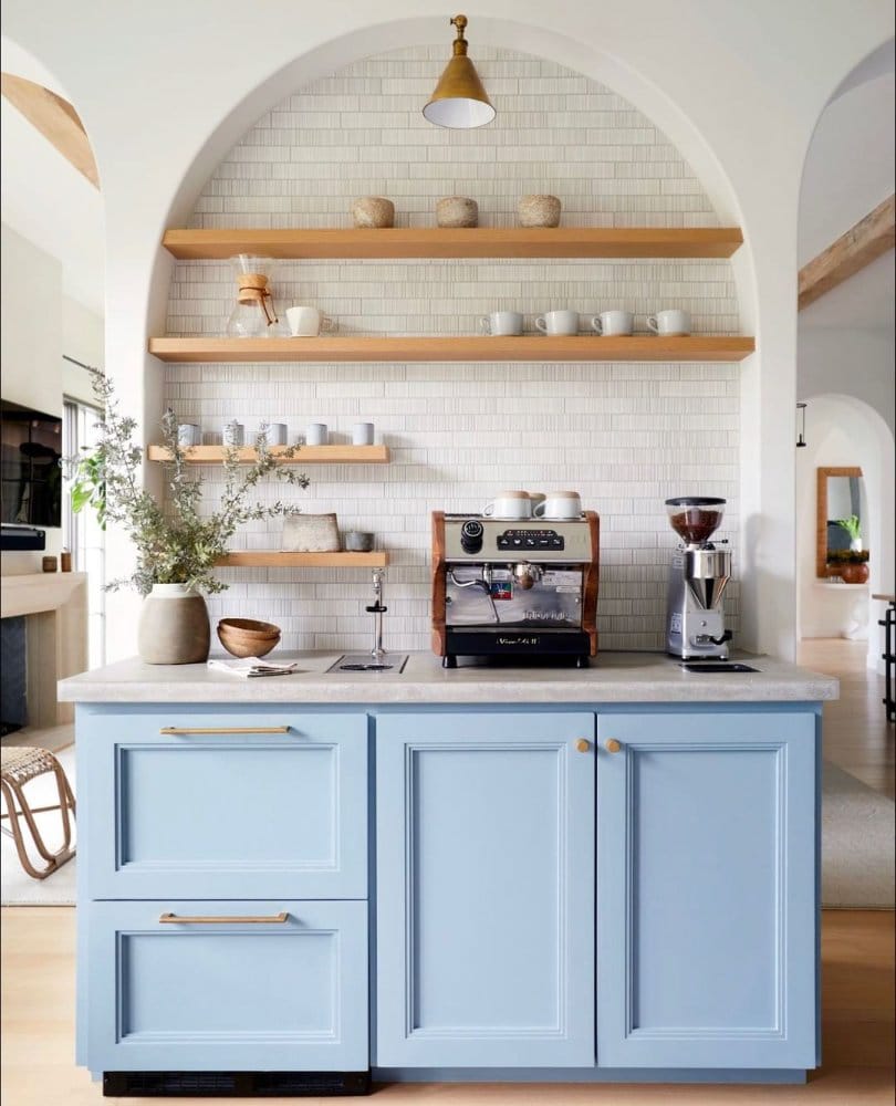 Light blue cabinetry coffee bar with an arched alcove, floating wooden shelves, and professional espresso machine and grinder.