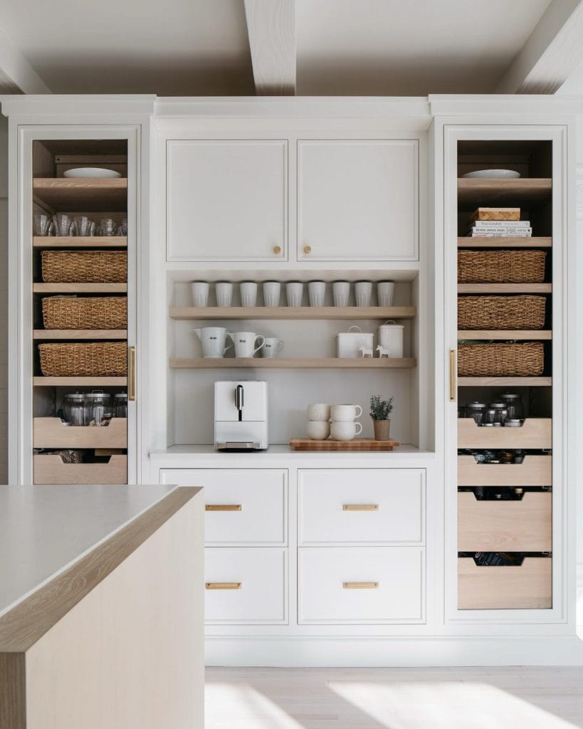 A minimalist coffee bar with white cabinetry, open shelves, and woven baskets. The sleek white coffee machine and neutral decor create a clean and organized space.