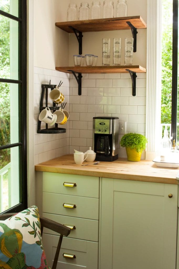 A compact coffee bar in a corner, with wooden shelves and a coffee machine. The space is bright and inviting, featuring mugs and glass jars for a cozy feel.