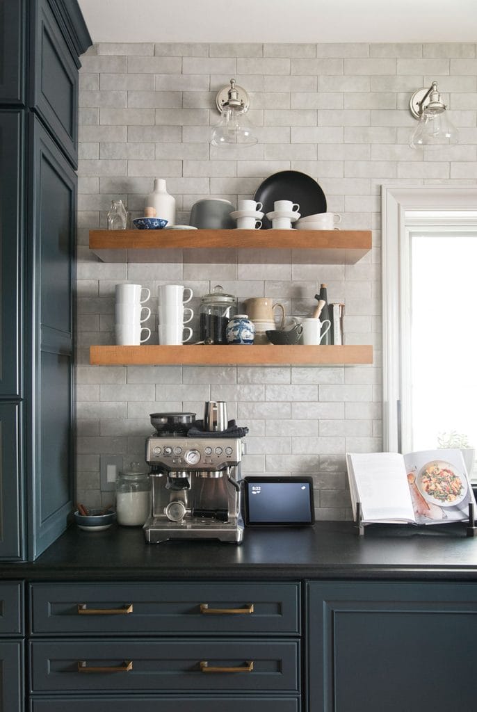 Coffee bar with dark cabinetry and a light, textured backsplash, wooden floating shelves, and a high-end espresso machine.