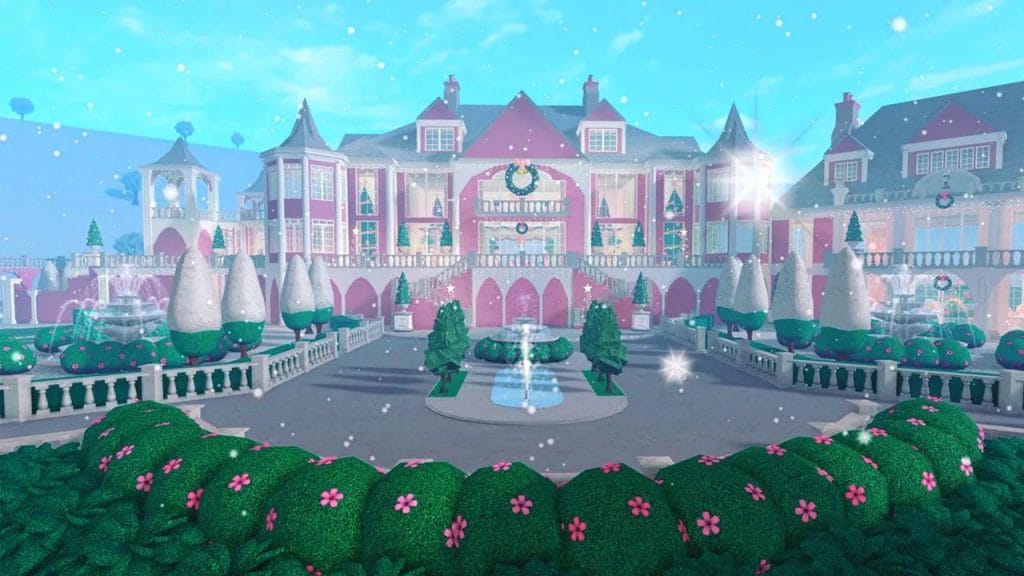 A festive pink mansion decorated for Christmas, featuring snow-covered trees, holiday wreaths, and a grand entrance with a fountain.