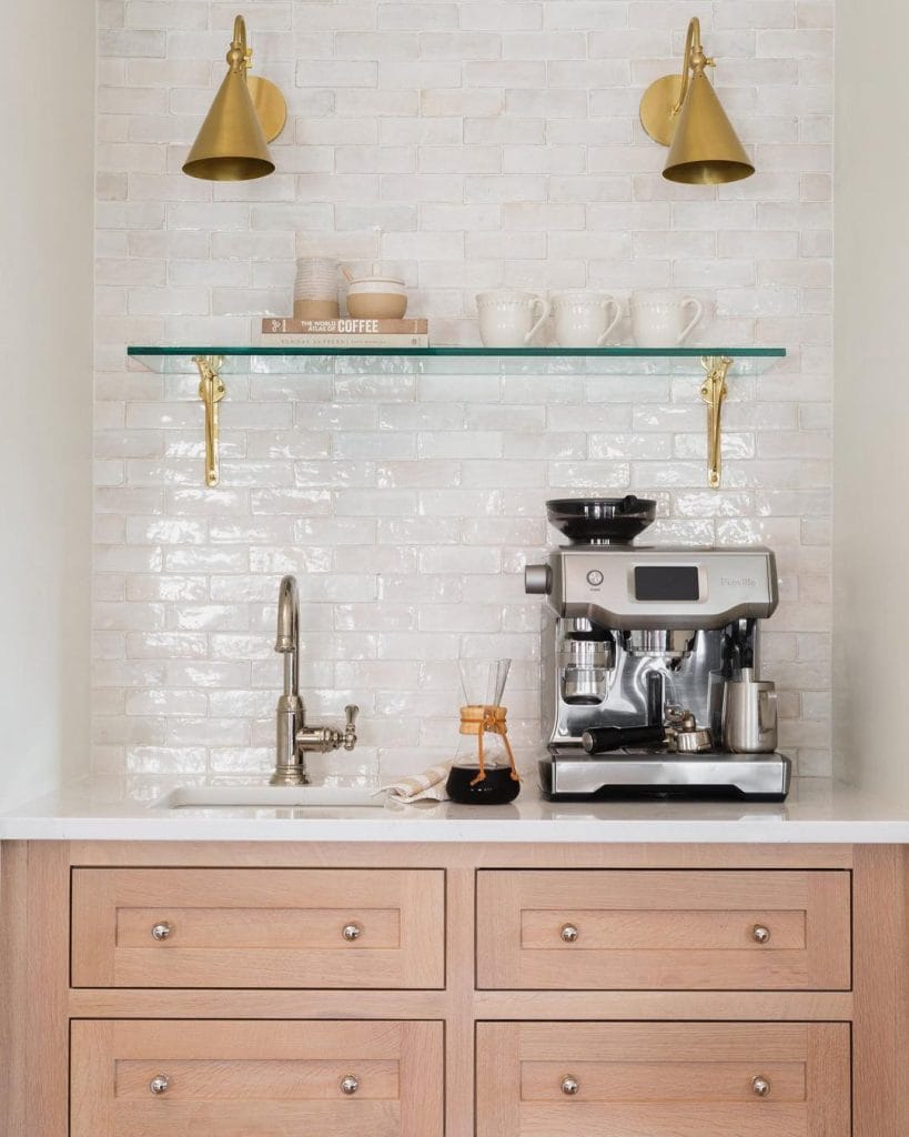 Coffee bar with light wood cabinetry, glass shelf, and brass sconces.