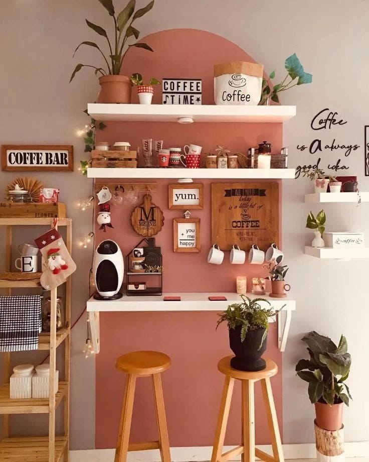 A stylish coffee bar setup with a pink accent wall and white shelves holding assorted mugs and decor items. The playful color scheme and organized display create a fun and inviting space.