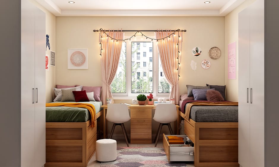 A bright dorm room with two beds, colorful bedding, a central desk, and string lights, creating a cheerful shared space.