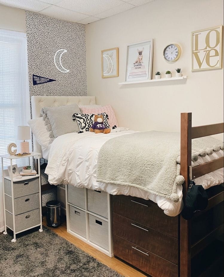 A minimalist dorm room with white and gray tones, moon wall art, and under-bed storage.
