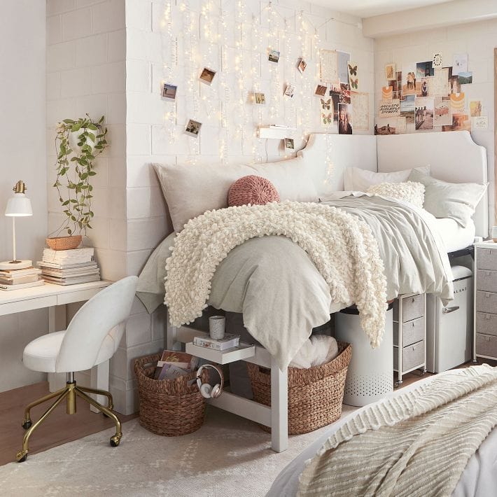 A dorm room with neutral tones, cozy bedding, a string light photo wall, and a minimalist desk setup.