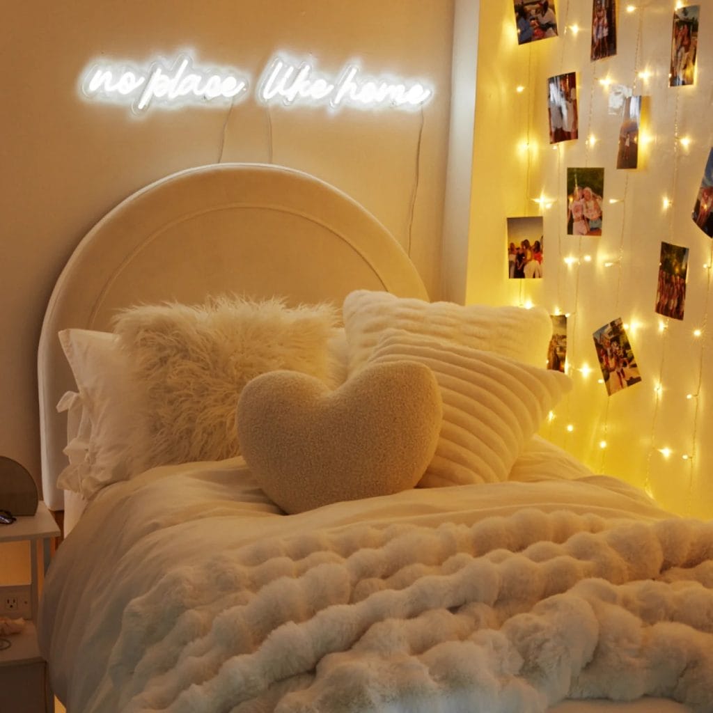 A cozy bed with warm lighting, fluffy pillows, and a neon sign.