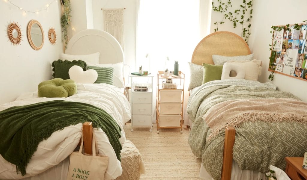 Shared dorm room with twin beds, green and white bedding, round mirrors, leafy garlands, and a personalized collage board for photos.