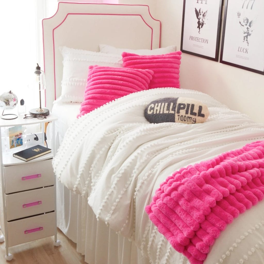 Bed with bright pink pillows and a "CHILL PILL" cushion, side table with essentials and a disco ball.