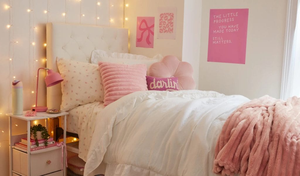 A bed with soft pink bedding and floral accents, adorned with fairy lights and decorative pillows.