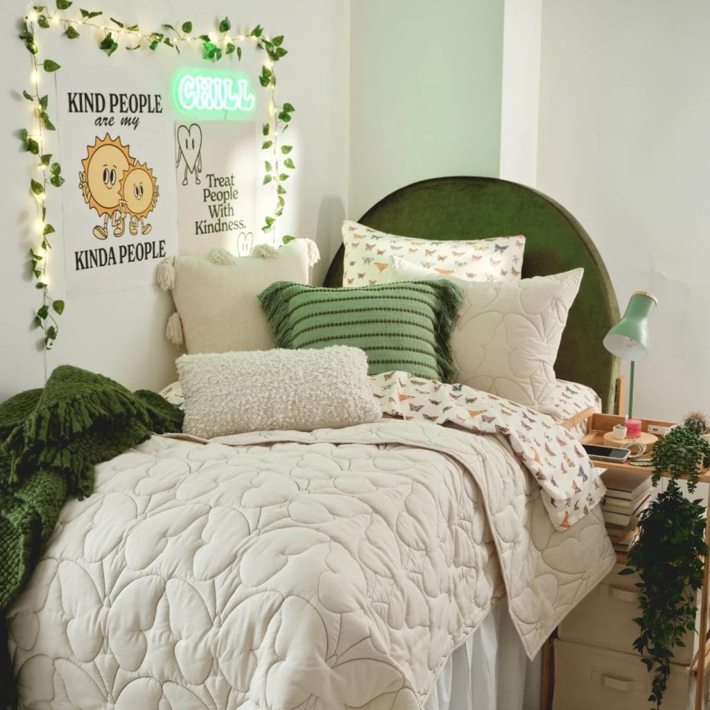 A cozy room with a green velvet headboard, white bedding, green accent pillows, and string lights with wall art.