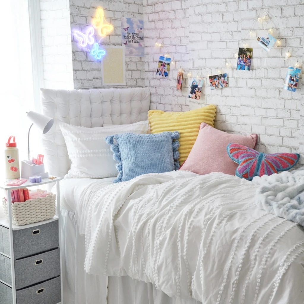 A bright room with a white bed, colorful pillows, neon butterfly lights, and string photo lights.