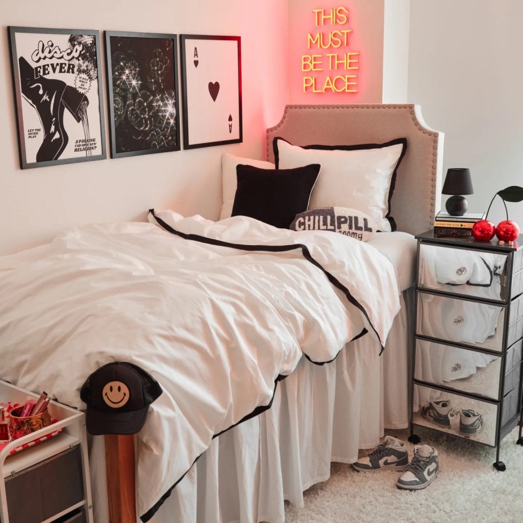 A cozy room with a white bed, black pillows, a neon sign, and black and white wall art.