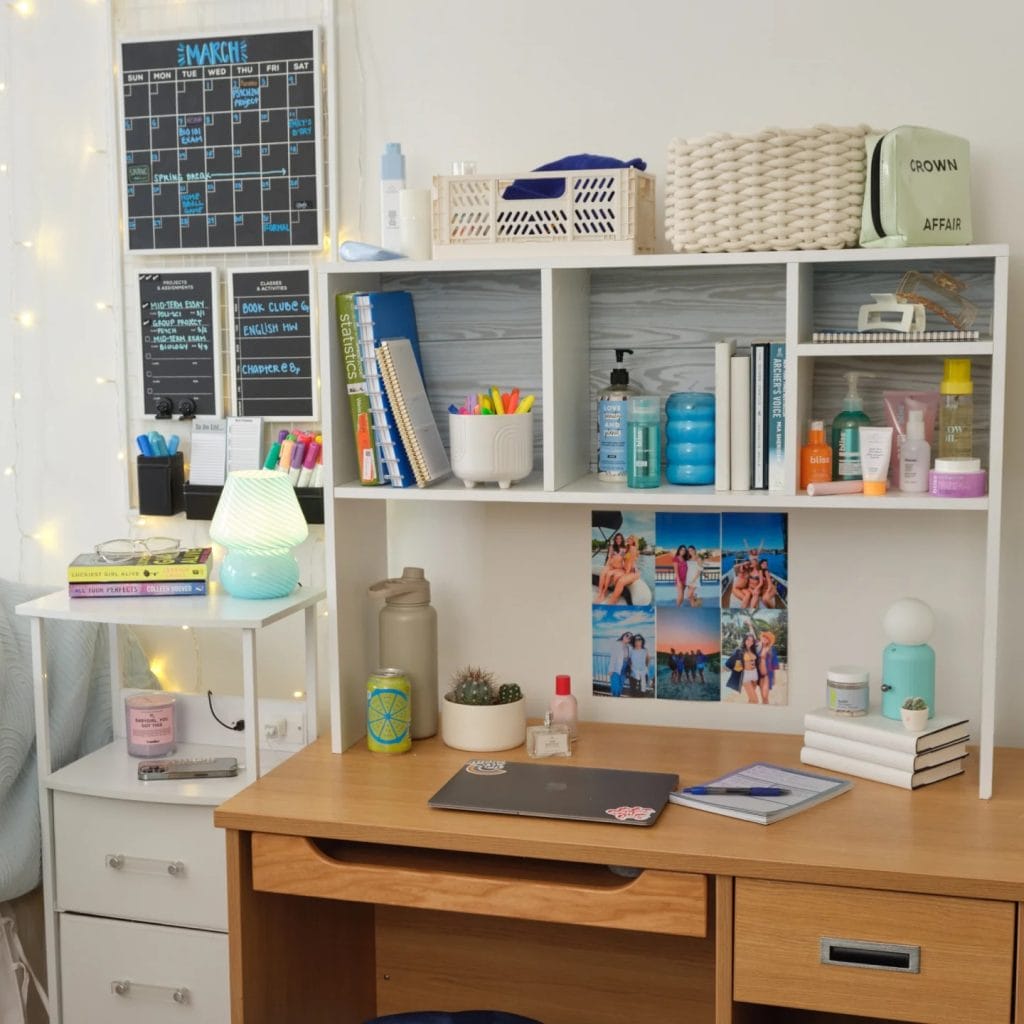 An organized study space with a wooden desk, shelves holding supplies, books, and decor, with a calendar and photo display.