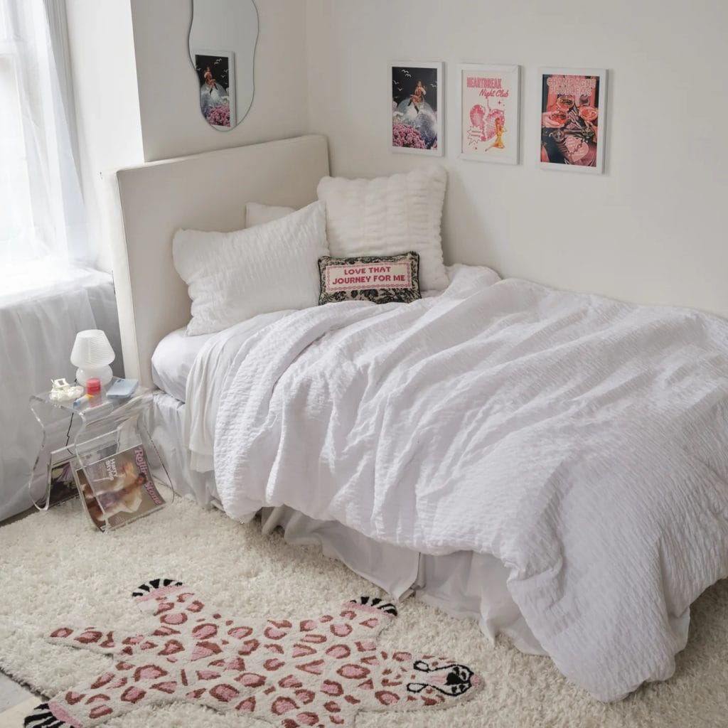 A minimalist room with a white bed, fluffy pillows, framed wall art, and a unique rug.