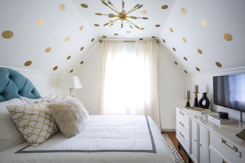 Teen bedroom with a sloped ceiling decorated with gold polka dots, blue headboard, and white bedding.