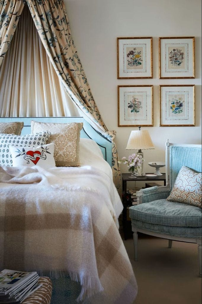 Vintage-style bedroom with floral drapes, a plush armchair, and framed botanical prints.