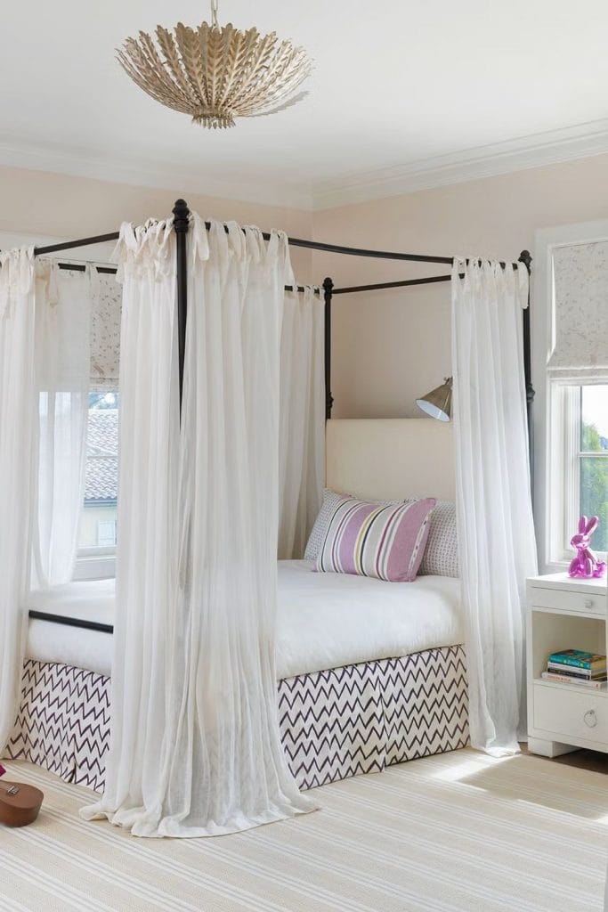 Bedroom with a canopy bed draped in white curtains and accented by neutral tones.