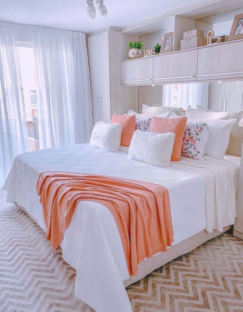 A bright space with a white bed, pink pillows, and a peach blanket, featuring built-in storage.