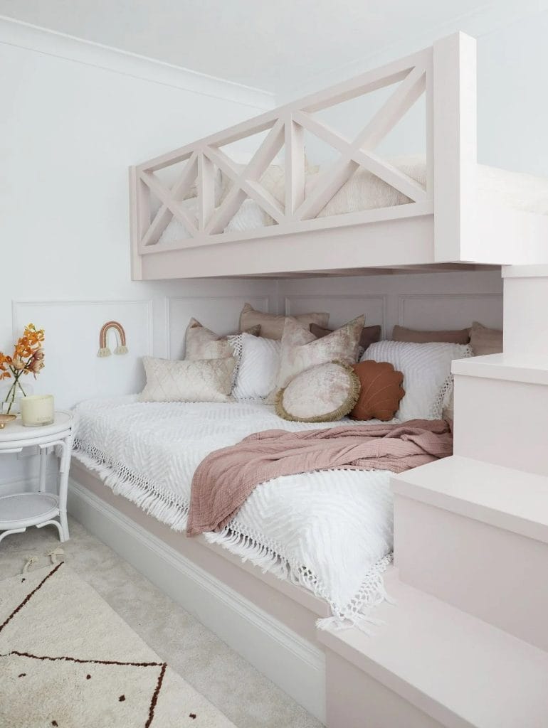 A space with a built-in loft bed, lower seating area, and pink and neutral decor.