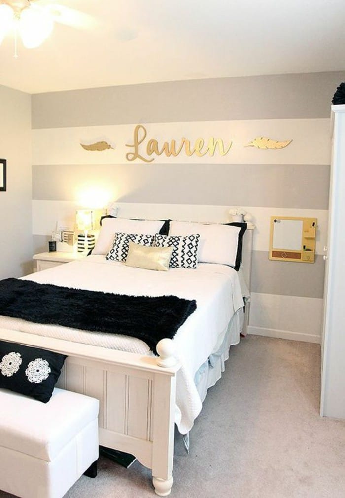 A space with a striped wall, name sign, black and white bedding, and gold accents.