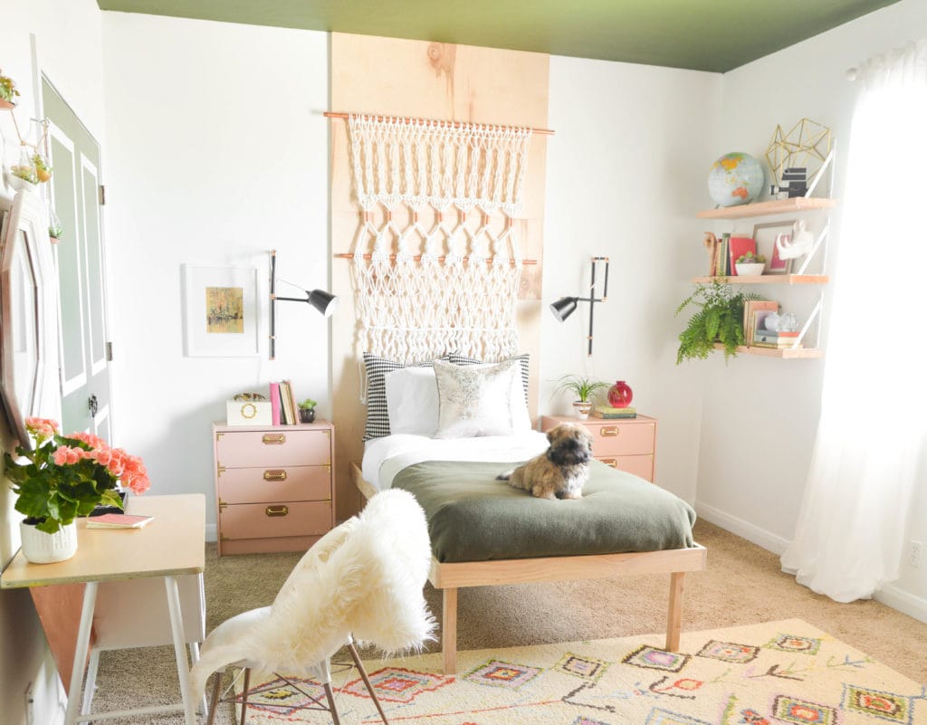 A space with a green ceiling, macramé wall hanging, wooden furniture, and lots of greenery.