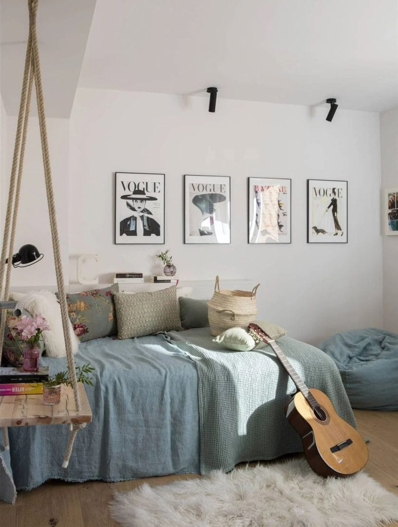 A space with fashion-inspired wall art, light blue linens, and a rustic wooden swing shelf.