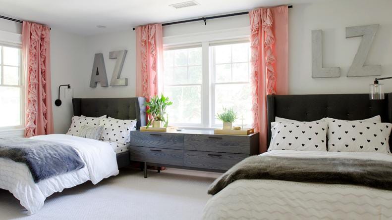 Shared teen bedroom with twin beds, pink curtains, and personalized initials on the wall.