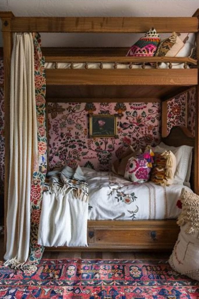 A cozy space with a wooden bunk bed, embroidered bedding, and floral wallpaper.