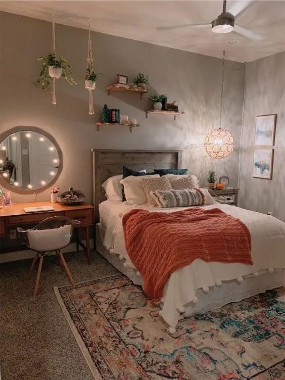 Cozy bedroom with earth tones, orange throw blanket, hanging plants, and soft lighting.