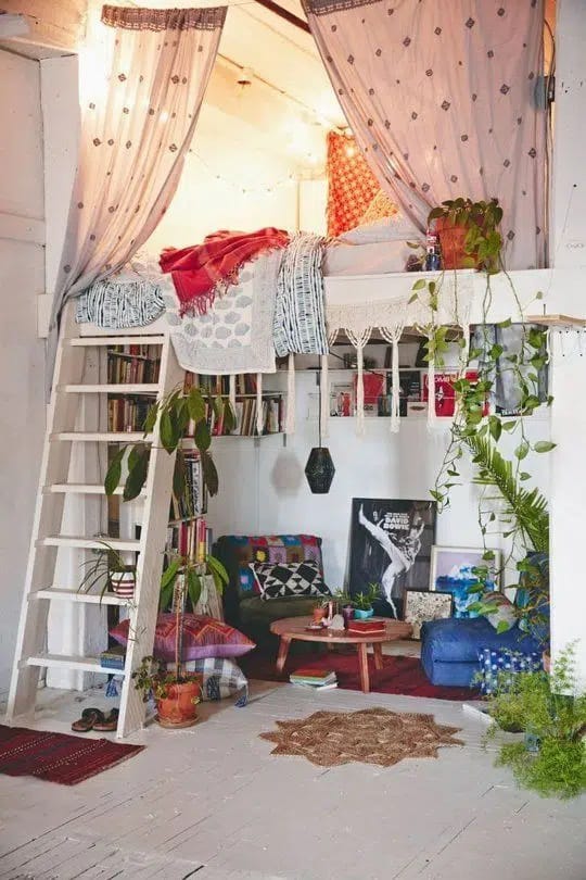 Loft-style bedroom with a raised bed, cozy seating area, and lots of plants.