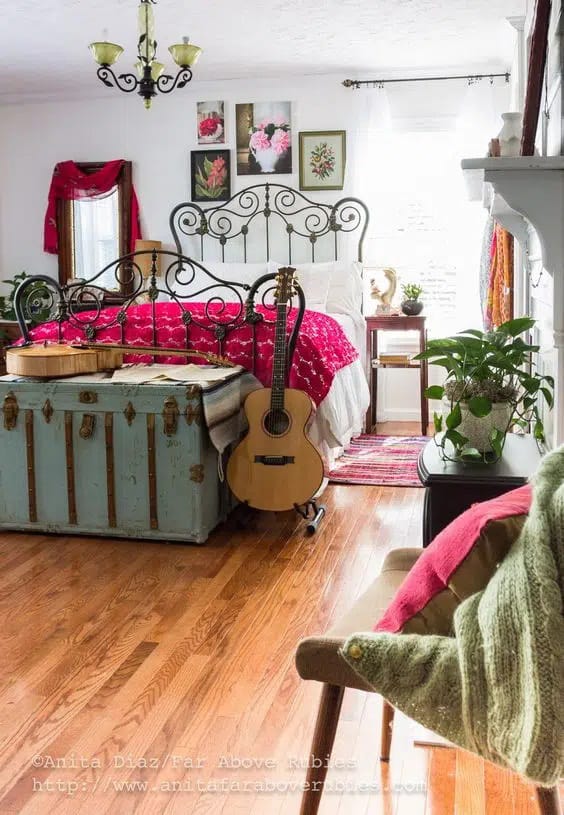 Rustic bedroom with an iron bed frame, distressed chest, and vibrant red bedding.