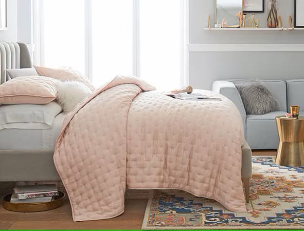 A bedroom with blush-colored bedding, a stylish rug, and a chic side table.