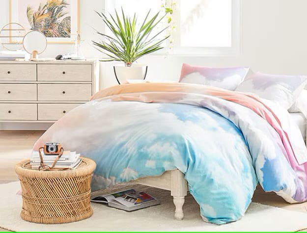 A bedroom with a sky-blue and white cloud-themed duvet cover, bright and airy decor, and a dresser.