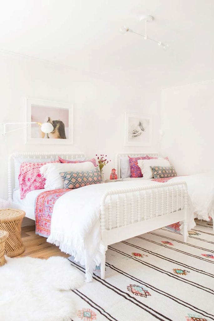 A twin bedroom with colorful bohemian-style pillows and throws on white beds, creating a bright and fun atmosphere.