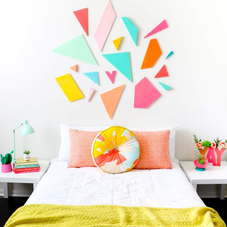 A bedroom with a geometric wall design made of colorful shapes, white bedding, and bright accent pillows.