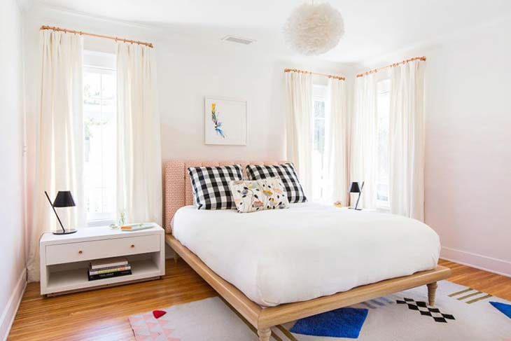 A minimalist bedroom with white bedding, black and white checkered pillows, and natural light.