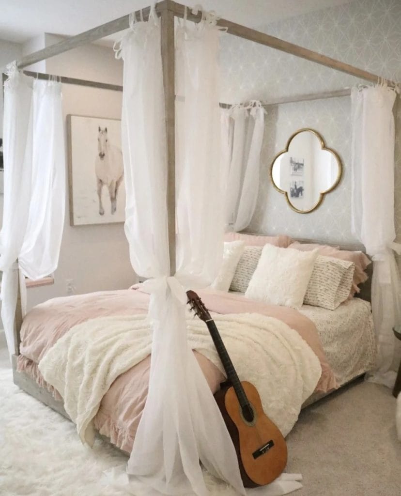 A bedroom with a four-poster bed, white curtains, soft bedding, and a guitar leaning against the bed.